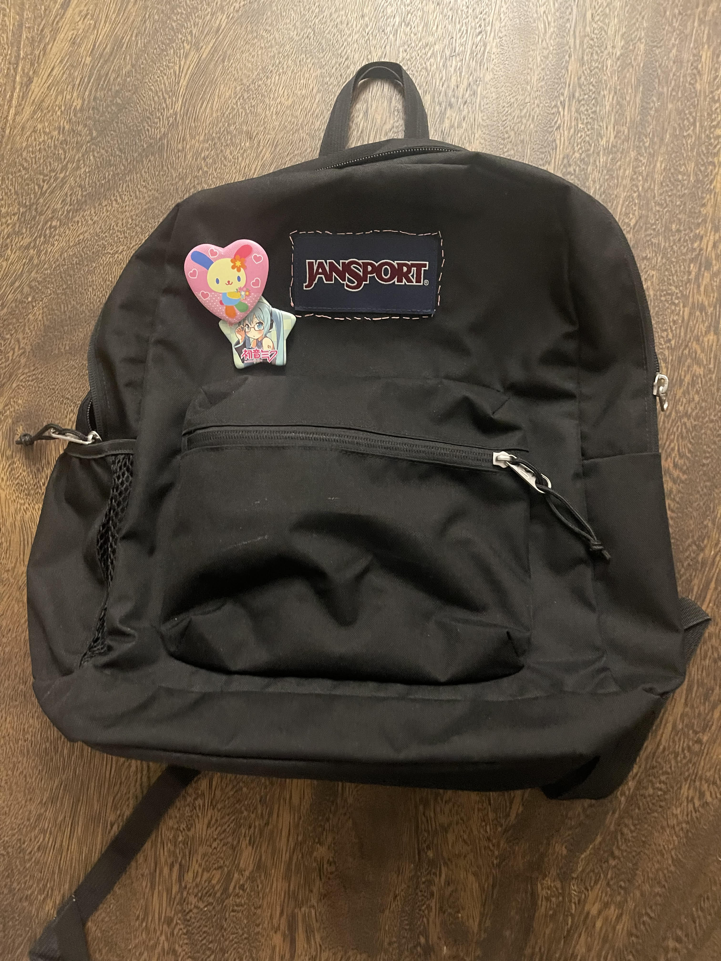 a black jansport with a heart shaped Usahana pin and a star shaped Hatsune Miku pin