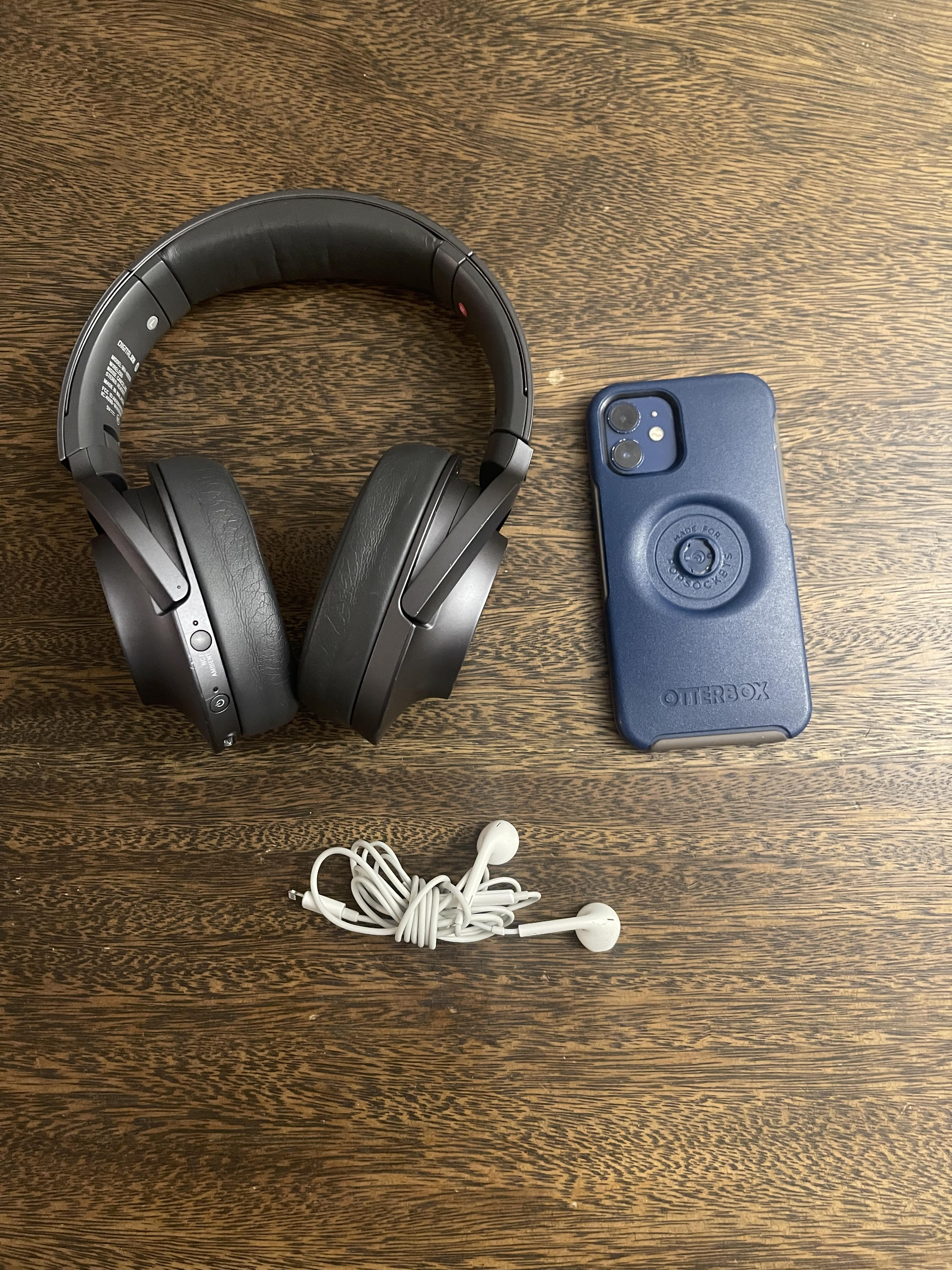 A pair of dark grey headphones, white earbuds, and a phone that has a blue and beige case.